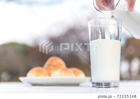 テラスのテーブルでピッチャーからグラスに牛乳を注ぐ朝食の風景 テラスのテーブルでピッチャーからグラスに牛乳を注ぐ朝食の風景 72335148
