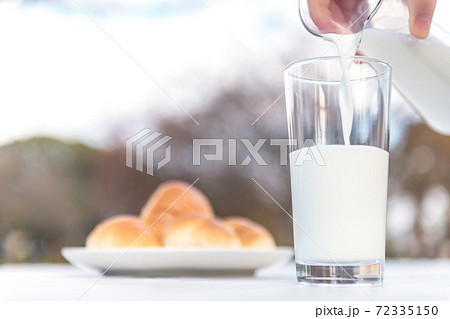 テラスのテーブルでピッチャーからグラスに牛乳を注ぐ朝食の風景 テラスのテーブルでピッチャーからグラスに牛乳を注ぐ朝食の風景 72335150