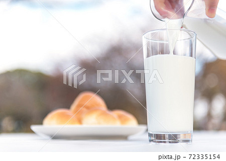 テラスのテーブルでピッチャーからグラスに牛乳を注ぐ朝食の風景 72335154