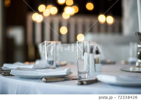 Table setting at a restaurant. Clean glass cup close up. Details of the banquet table. On the background blur are burning garlands with light bulbs Table setting at a restaurant. Clean glass cup close up. Details of the banquet table. On the background blur are burning garlands with light bulbs 72338426