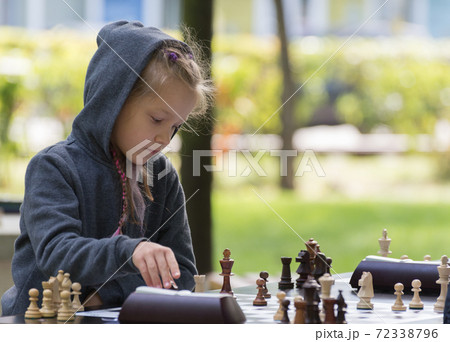 Smart Girl, seven years old is taking part a kids chess tournament outdoor in the park. 72338796