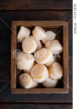 Raw uncooked scallops, flat lay, on dark wooden background Raw uncooked scallops, flat lay, on dark wooden background 72351856