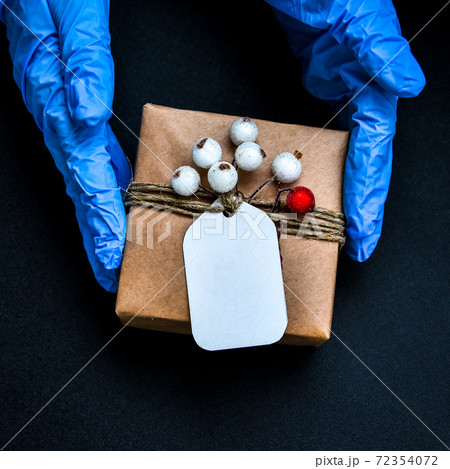 Holiday shopping. Festive gifts. Pandemic restriction. Winter shopping. Hand in protective gloves holding present zero waste box. Advertising background. Pandemic. Stay safe. Holiday shopping. Festive gifts. Pandemic restriction. Winter shopping. Hand in protective gloves holding present zero waste box. Advertising background. Pandemic. Stay safe. 72354072