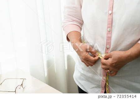 Senior woman measuring her waist by measuring tape Senior woman measuring her waist by measuring tape 72355414