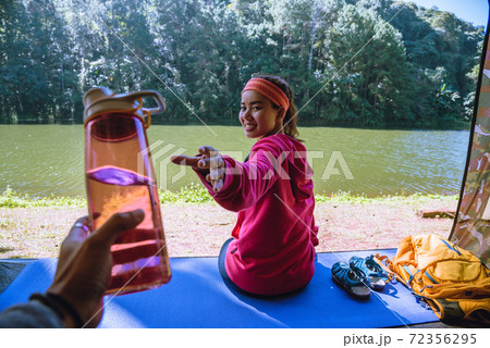 Young man submitting a bottle of drinking water to lover at camping tent facial. 72356295