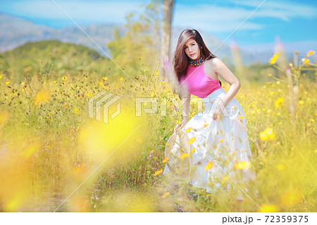 Asian beautiful woman, long hair in pink dress on yellow cosmos filed in winter with blue sky and mountain. Beautiful cute girl portrait with flowers in background. Travel in nature outdoor concept Asian beautiful woman, long hair in pink dress on yellow cosmos filed in winter with blue sky and mountain. Beautiful cute girl portrait with flowers in background. Travel in nature outdoor concept 72359375