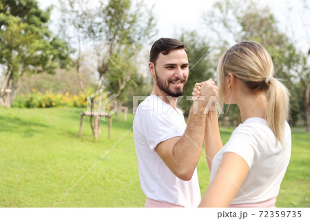 image of young caucasian couple in white and pink sport dress with smiling and arm wrestling challenge in the park with green tree in nature image of young caucasian couple in white and pink sport dress with smiling and arm wrestling challenge in the park with green tree in nature 72359735