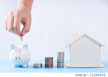 Hand putting money coin into piggy bank with wooden house and stack coins isolated grey background. Property investment and house mortgage financial concept. Hand putting money coin into piggy bank with wooden house and stack coins isolated grey background. Property investment and house mortgage financial concept. 72364039