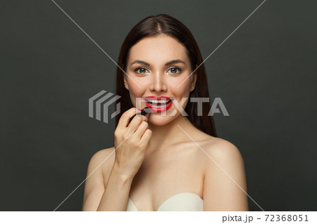 Lovely woman applying red lipstick on lips on black background Lovely woman applying red lipstick on lips on black background 72368051
