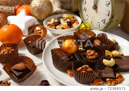 sweet food background for christmas or holiday decoration - chocolate candies, tangerines, nuts and dried fruits on white wood 72369571