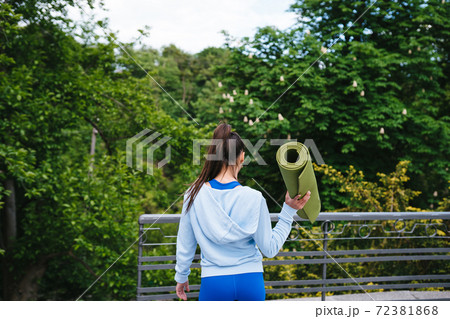 Young woman walking in urban park holding fitness rug. Young woman walking in urban park holding fitness rug. 72381868