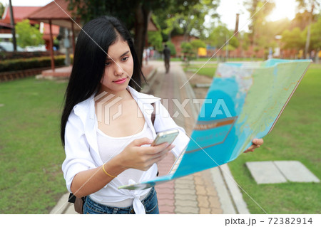 Young asian traveler using cell phone and holding map in temple while traveling during holiday vacation Young asian traveler using cell phone and holding map in temple while traveling during holiday vacation 72382914