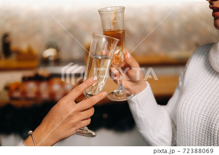 two girls in a cozy home environment with champagne in their hands at Christmas. Smiling girls drink champagne on a festive evening 72388069