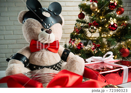 toy bear dressed in leather straps harness accessory for BDSM on the background of the Christmas tree toy bear dressed in leather straps harness accessory for BDSM on the background of the Christmas tree 72390323