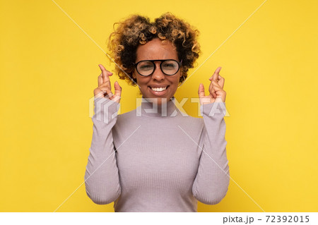 Cheerful African American woman awaits for miracle, prays and hopes dreams come true, crosses fingers for good luck 72392015