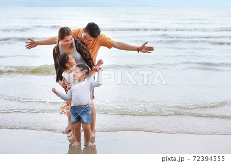 happy asian family dad and mom with their children boy and girl raising hands with happy smiling face while standing on sandy beach during sunny day 72394555