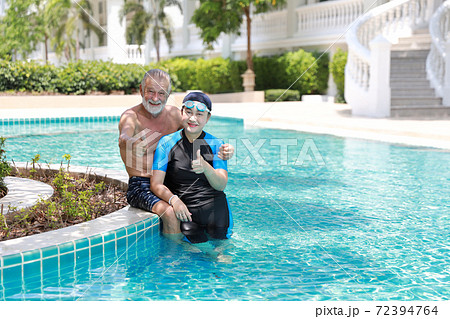 happy elderly caucasian husband and elderly asian wife take a break while swimming in pool during retirement holiday with relaxation and smiling while showing thumb up or like and looking at camera happy elderly caucasian husband and elderly asian wife take a break while swimming in pool during retirement holiday with relaxation and smiling while showing thumb up or like and looking at camera 72394764