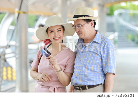 asian traveler couple husband and wife in pink and blue shirt with white nice hat and luggage walking in downtown with happy smiling face while showing credit card for shopping during retirement age asian traveler couple husband and wife in pink and blue shirt with white nice hat and luggage walking in downtown with happy smiling face while showing credit card for shopping during retirement age 72395301