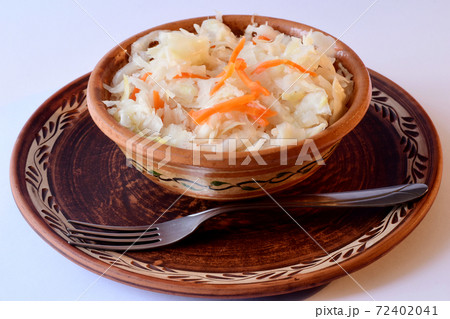 Sauerkraut with carrots in a clay plate and a fork are on the table. Sauerkraut with carrots in a clay plate and a fork are on the table. 72402041