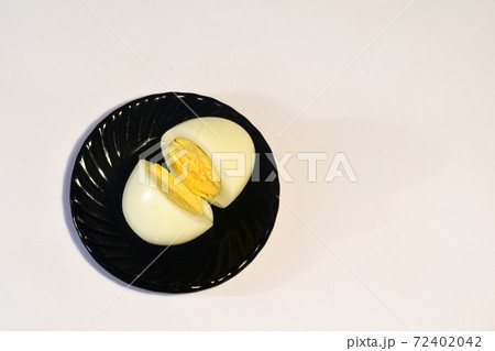 A peeled and cut chicken egg lies on a dark plate A peeled and cut chicken egg lies on a dark plate 72402042