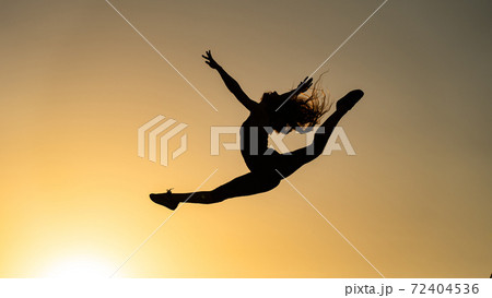 Female flexible dancer jumping during sunset on the orange sky background. Concept of freedom and happiness  72404536