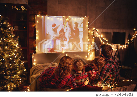 family mother father and children watching projector, film, movies with popcorn in   christmas evening   at home. 72404903