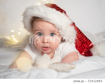 Adorable baby girl in Santa hat lying on the bed Adorable baby girl in Santa hat lying on the bed 72412883