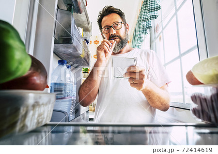 Adult caucasian man taking note list of food looking inside the open fridge at home - kitchen activity and alternative point of view - market shopping and quarantine lockdown stayhome coronavirus time Adult caucasian man taking note list of food looking inside the open fridge at home - kitchen activity and alternative point of view - market shopping and quarantine lockdown stayhome coronavirus time 72414619
