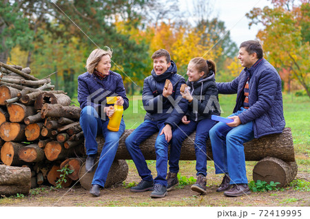 family relaxing outdoor in autumn city park, happy people together, parents and children, they drink tea and eat sandwiches, talking and smiling, beautiful nature 72419995