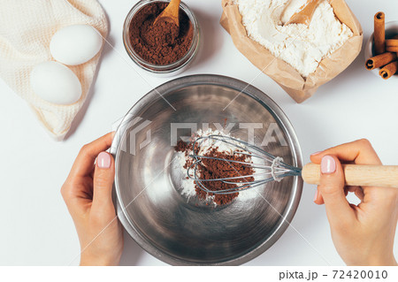 Top view of female hands whisk flour and cocoa powder Top view of female hands whisk flour and cocoa powder 72420010