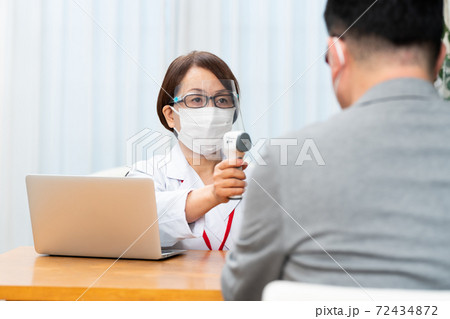 フェイスシールドを付けて検温をする看護師 72434872