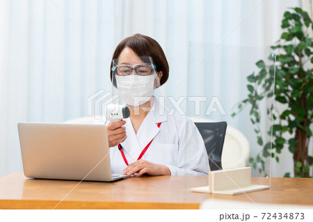フェイスシールドを付けて検温をする看護師 72434873