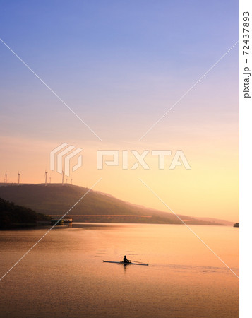 Sunset landscape of lake with evening sunlight and man rowing canoe across the lake. 72437893