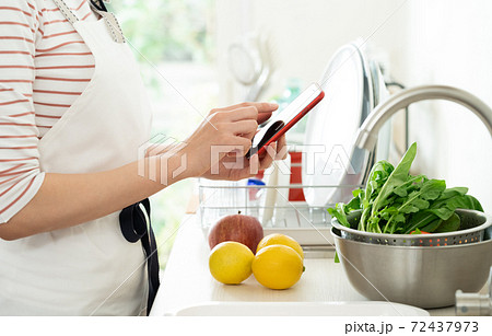 キッチンでスマホを見る女性の手元 72437973