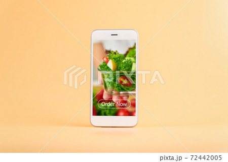 Smartphone on the orange background and show application screen for ordering salad online. Smartphone on the orange background and show application screen for ordering salad online. 72442005