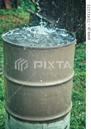Rain barrel. Strong stream of water pours into an old metal barrel during heavy rain 72451223