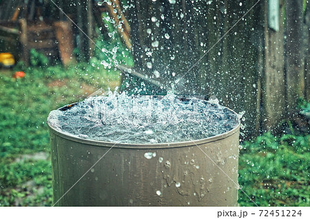 Rain barrel. Strong stream of water pours into an old metal barrel during heavy rain 72451224