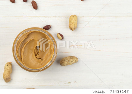 Jar of peanut butter on a white wooden table with nuts scattered nearby. Space for text. Jar of peanut butter on a white wooden table with nuts scattered nearby. Space for text. 72453147
