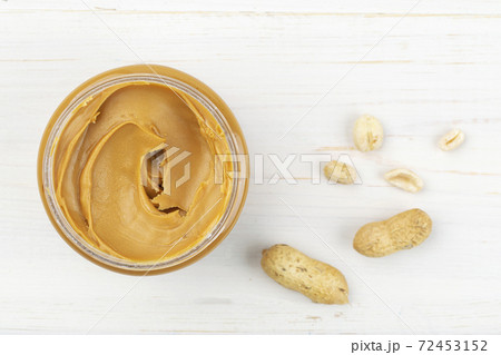 Jar of peanut butter on a white wooden table with nuts scattered nearby. Space for text. Jar of peanut butter on a white wooden table with nuts scattered nearby. Space for text. 72453152