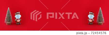 Christmas tree and ceramic statuette of Ox in medical mask on red background. Wide banner with copy space. Symbol of new year 2021. 72454576