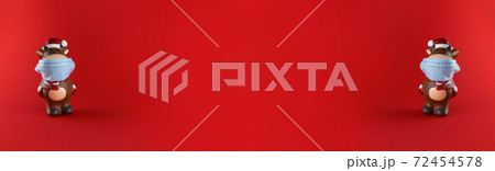 Ceramic statuettes of Ox in medical mask on red background. Wide banner with copy space. Symbol of new year 2021. Ceramic statuettes of Ox in medical mask on red background. Wide banner with copy space. Symbol of new year 2021. 72454578