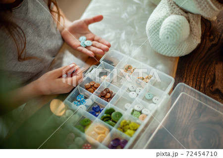 Little cute girl chooses buttons for knitted snowmen. New Year's decor is on the table. Preparation for Christmas concept. 72454710