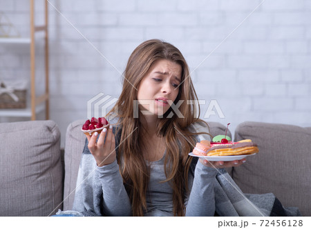 Depressed young lady having eating disorder, comforting herself with sweets on sofa at home 72456128