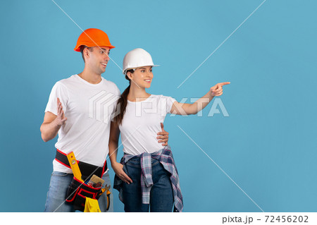 Excited young couple in protective hard hats pointing aside at copy space Excited young couple in protective hard hats pointing aside at copy space 72456202