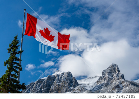 Close up of National Flag of Canada with natural mountains and trees scenery in the background. Close up of National Flag of Canada with natural mountains and trees scenery in the background. 72457185