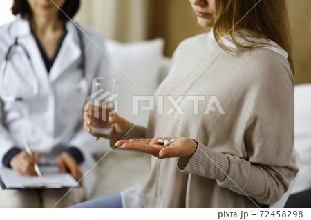 Close-up woman-patient holding pills near her doctor, time to take medications, cure for headache or remedy pain killer drugs. Stay at home concept during Coronavirus pandemic and self isolation 72458298