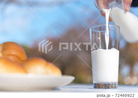 テラスのテーブルでピッチャーからグラスに牛乳を注ぐ朝食の風景 72460922