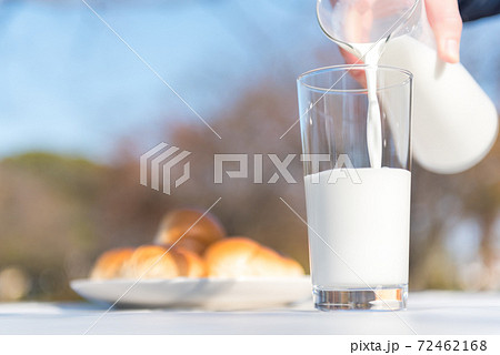 テラスのテーブルでピッチャーからグラスに牛乳を注ぐ朝食の風景 72462168