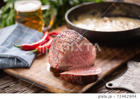 Rare cooked rump steak on a curring board nextto mushroom sauce, chillies and a beer 72462904
