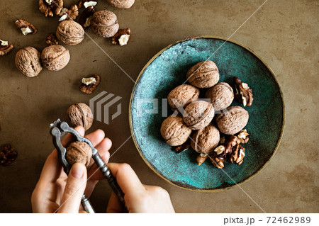 Woman's hands peeling walnuts with a nutcracker on a table, overhead view Woman's hands peeling walnuts with a nutcracker on a table, overhead view 72462989